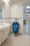 Blue 'Out of Order' sign on a wall-mounted trash can in a hospital bathroom.